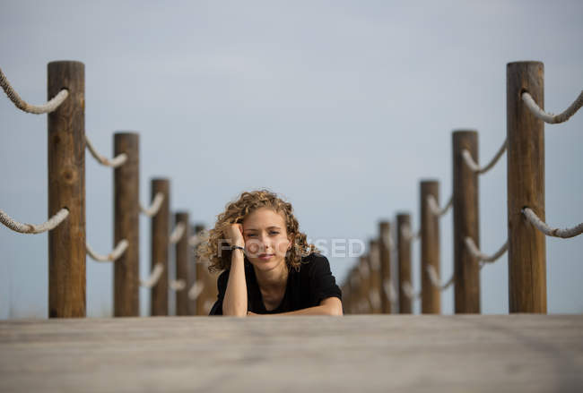 Молода жінка лежить спереду на дерев'яному пішохідному мосту в природі і дивиться на камеру — стокове фото