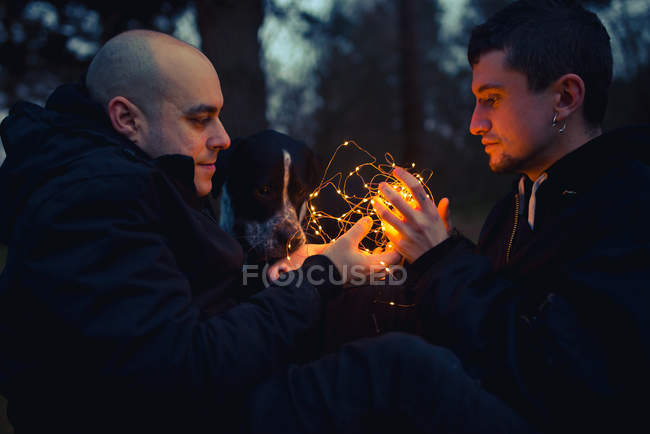 Гомосексуальна пара з підсвіченими казковими вогнями, сидячи в дрімотному лісі ввечері — стокове фото