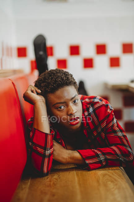 Confident African American woman lying on seats in cafe and looking at camera — Stock Photo