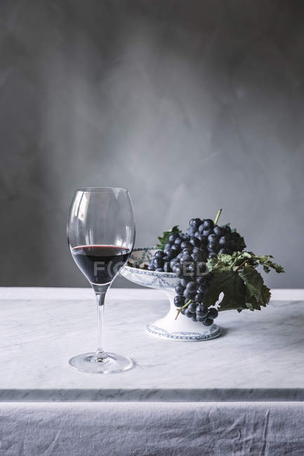 Ramo de uvas en plato y copa de vino en mesa - foto de stock