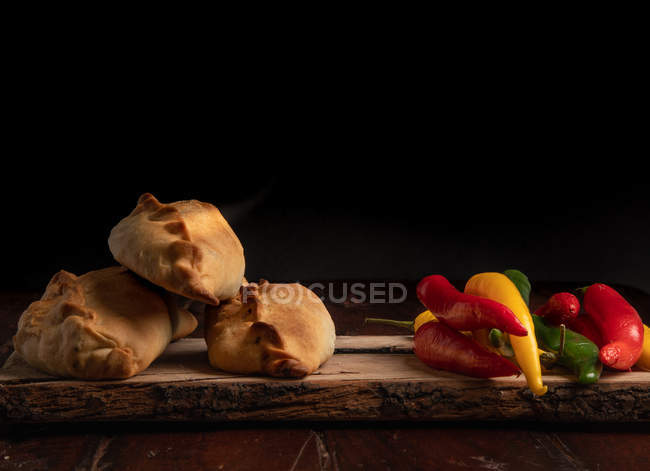 Домашні пиріжки і свіжий зелений і червоний перець чилі на дерев'яному столі на темному фоні — стокове фото