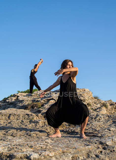 Jóvenes bailarinas misteriosas en negro llevan bailando sobre rocas en un día soleado - foto de stock