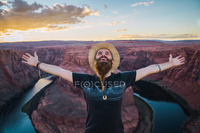 Человек, простирающий руки возле величественного каньона против облачного голубого неба во время путешествия по западному побережью США — стоковое фото