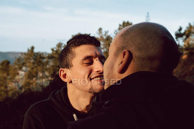 Side view of cheerful homosexual couple going to kiss on route in forest in sunny day — Stock Photo