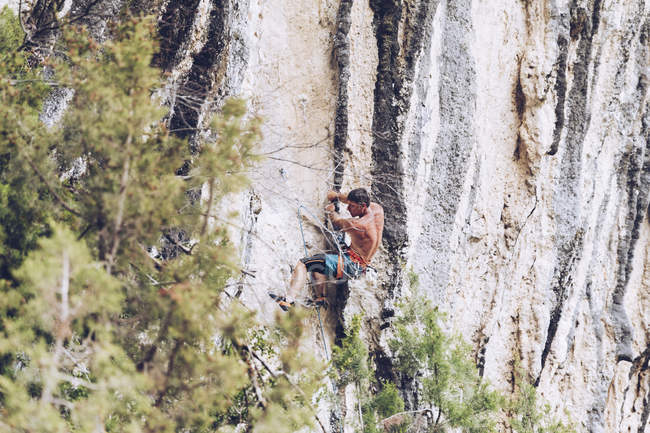Вид збоку на невпізнаваного чоловіка в шортах, що піднімаються вгору по скелі в сонячний день в сільській місцевості — стокове фото