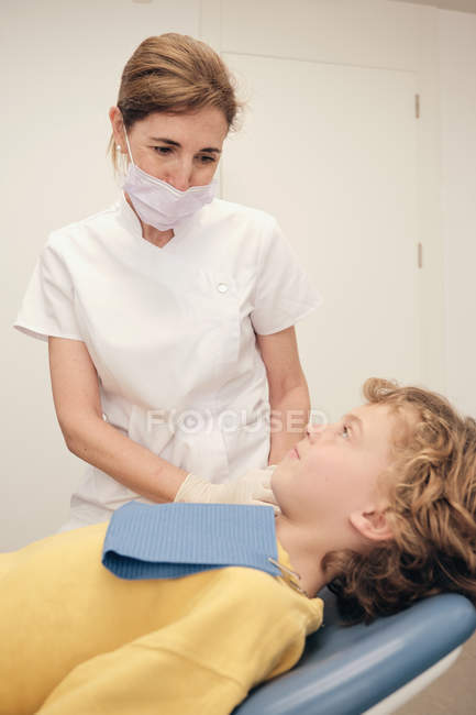 Femme en uniforme de médecin parlant à un petit patient dans un cabinet de dentiste — Photo de stock