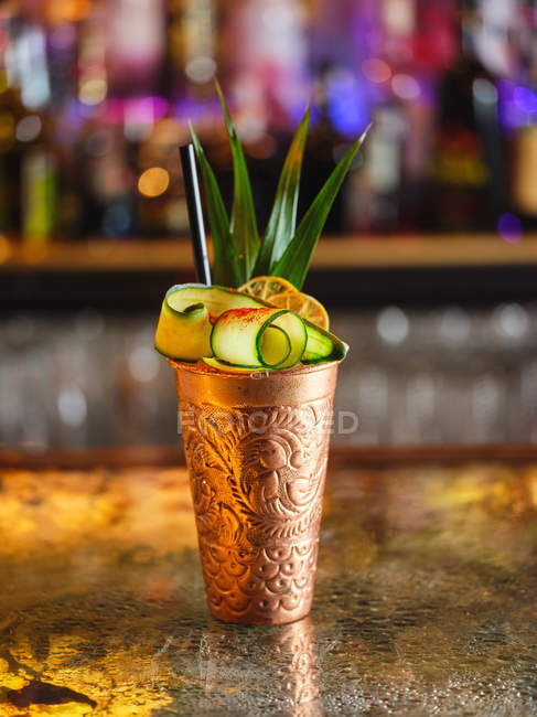 Tazza ornamentale di gustoso cocktail con frutta tropicale posto sul bancone in su sfondo sfocato di bar — Foto stock