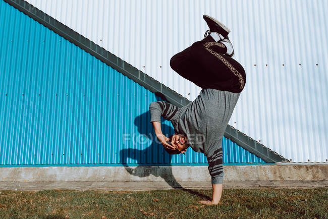 Young guy performing handstand and looking at camera while dancing near wall of modern building on city street — Stock Photo