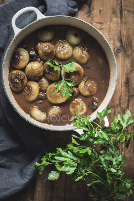 From above cooking pot with Boeuf Bourgingnon with mushrooms and green herbs on wooden table — Stock Photo