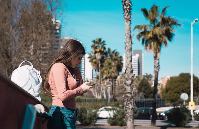 Adolescente regardant son smartphone dans la rue par une journée ensoleillée — Photo de stock