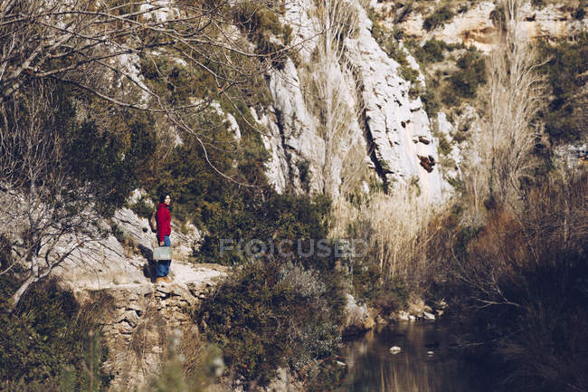 Donna con zaino e custodia in piedi sulla costa rocciosa del lago in maestose scogliere selvagge — Foto stock