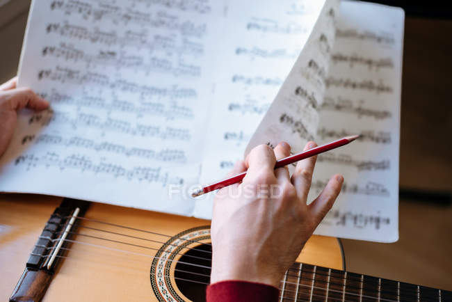 Crop man hands with sheet music playing guitar during rehearsal in studio. — Stock Photo