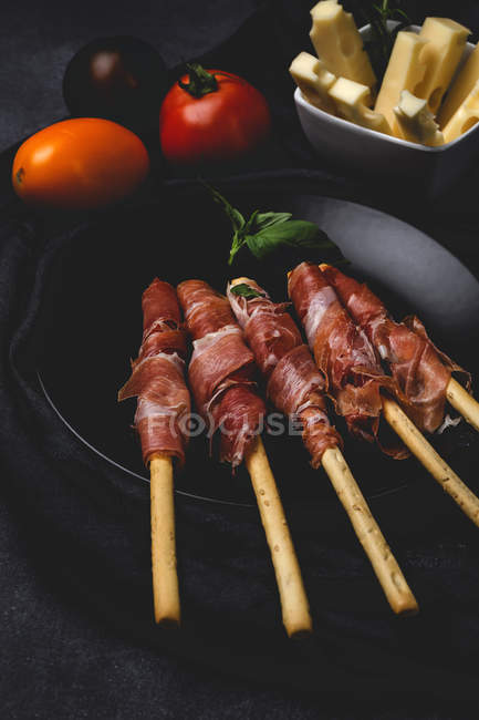 Грессини с испанской типичной ветчиной серрано на черной тарелке со свежими помидорами и сыром — стоковое фото