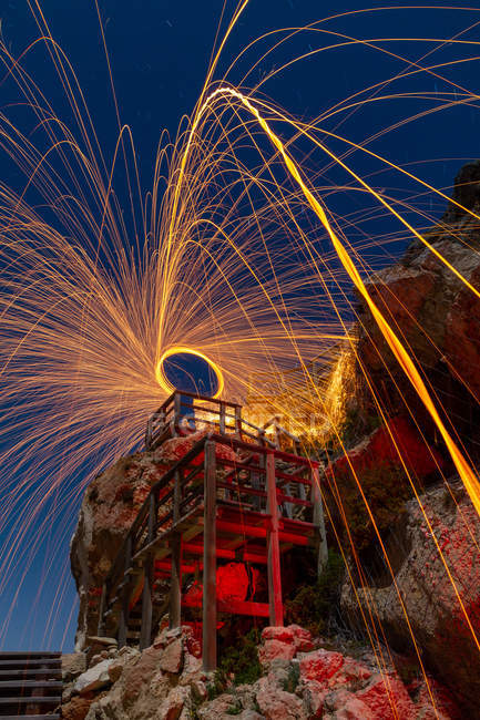 Lange Belichtung der Silhouette des Menschen mit brennenden runden und Feuerwerk auf Felsen — Stockfoto