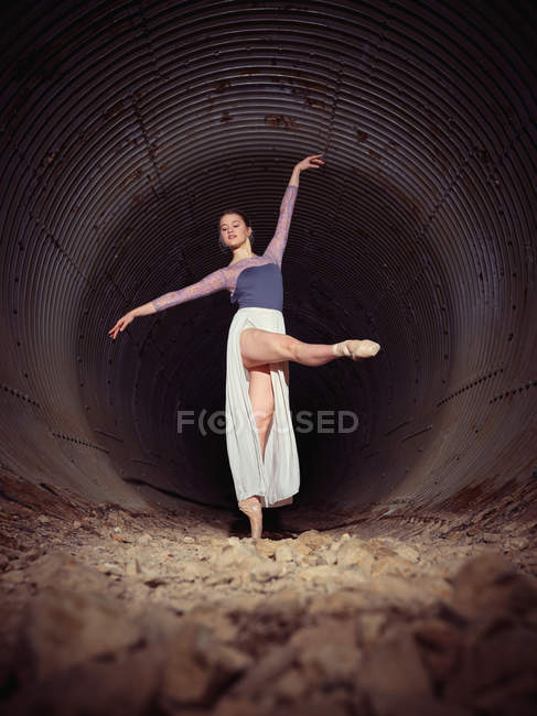 Slim joven mujer graciosamente girando mientras baila ballet dentro de tubería oxidada - foto de stock