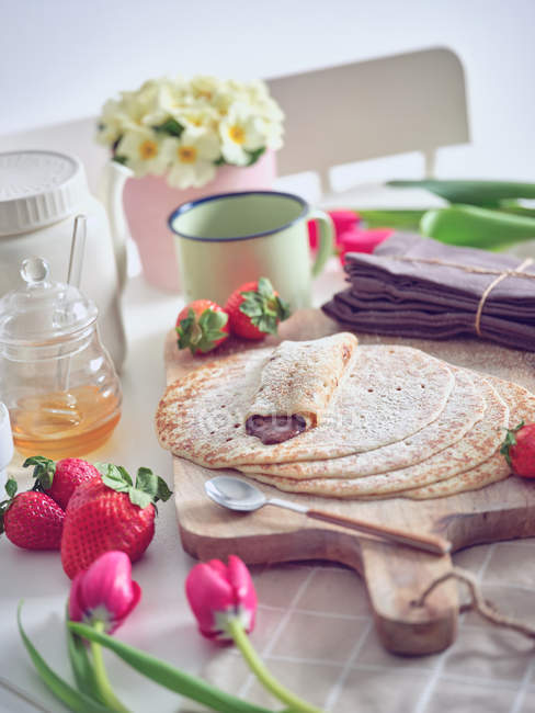 Завтрак с блинами и клубникой на кухонном столе с цветами — стоковое фото