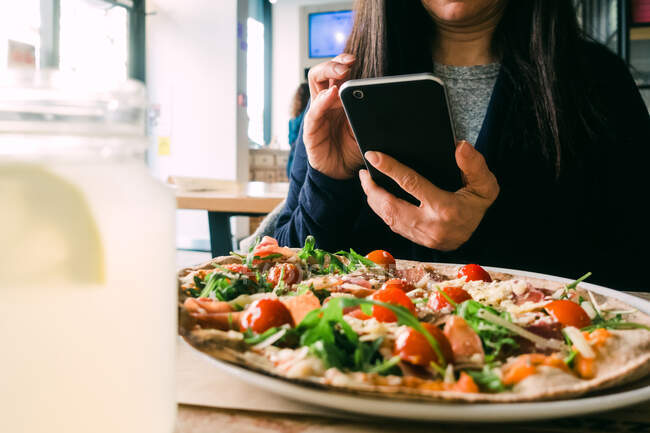 Erntehelferin nutzt Handy und sitzt mit leckerem Salat im Café am Tisch — Stockfoto