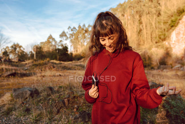 Junge lächelnde Hipster-Frau hört Musik mit Handy und geht in der Natur spazieren — Stockfoto