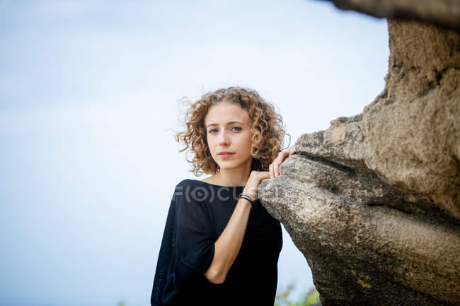 Junge ernste Frau lehnt sich an Felsen in der Natur und blickt in die Kamera — Stockfoto