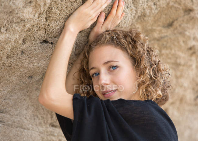 Молодая улыбающаяся женщина с поднятыми руками смотрит в камеру возле скалы — стоковое фото