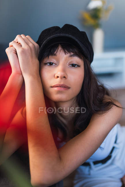 Young charming brunette woman in cap looking at camera in red smoke — Stock Photo