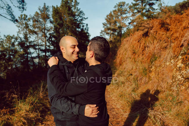 Laughing homosexual couple hugging on path in mountains in sunny day — Stock Photo