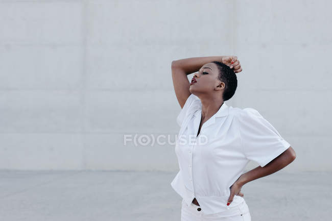 Sensuale donna etnica dai capelli corti moda in camicia bianca posa contro muro grigio — Foto stock