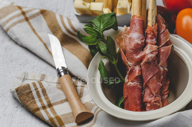 Gressini con tipico prosciutto serrano spagnolo in vaso con erba e coltello su stoffa — Foto stock