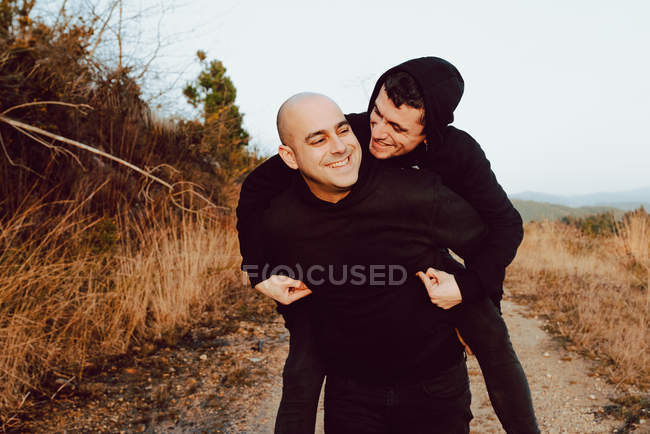 Feliz pareja homosexual divirtiéndose en ruta entre plantas en las montañas - foto de stock