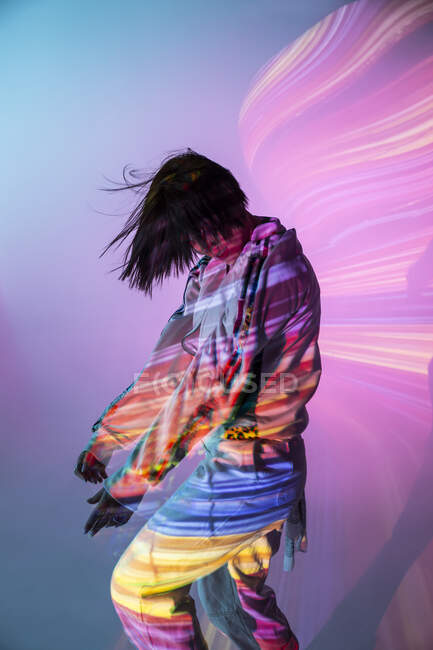 Side view of young woman in trendy outfit dancing under colorful illumination — Stock Photo