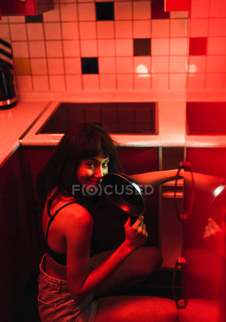 Sensuale giovane donna bruna in lingerie guardando la fotocamera e tenendo in mano la padella in cucina tra il rossore — Foto stock