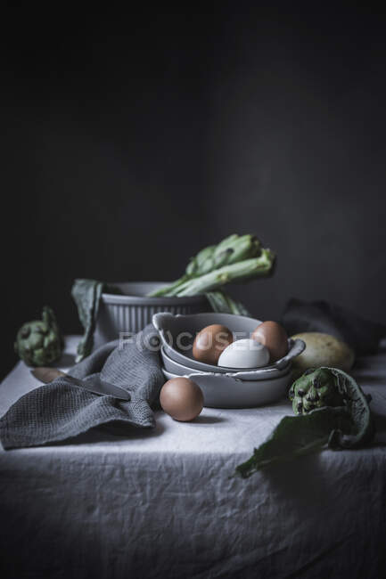 Eggs and different herbs in bowls placed on rustic table — Stock Photo