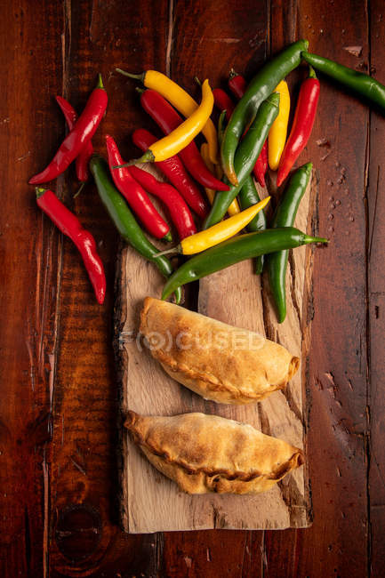 Homemade baked patties and fresh green and red chili peppers on board on brown wooden table — Stock Photo