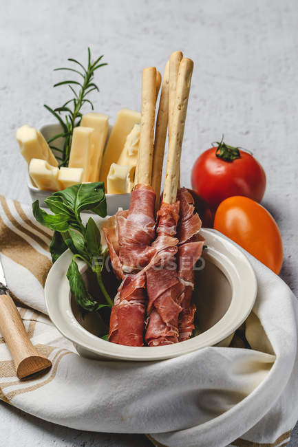 Gressinis with spanish typical serrano ham in pot with herb, cheese and fresh tomatoes on cloth — Stock Photo
