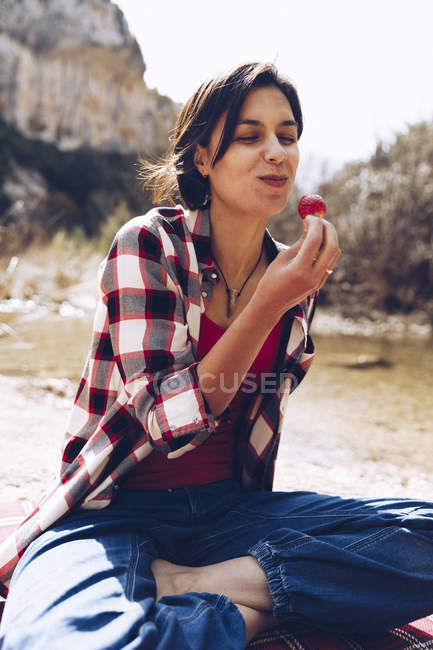 Crop man lying on plaid with woman sitting near and biting strawberry up enjoying time together on picnic in nature — Stock Photo