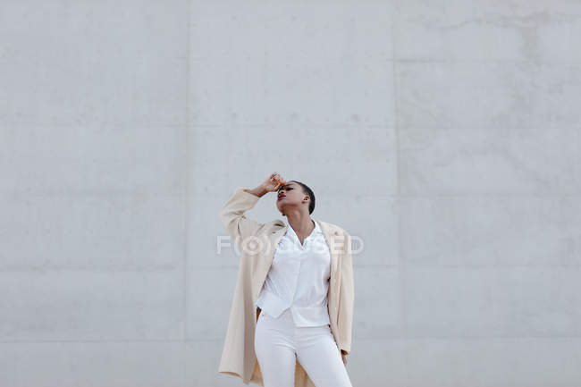 Modelo de pelo corto de moda en traje blanco posando contra pared gris - foto de stock