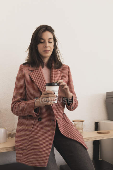Attrayant jeune femme tenant tasse de boisson et assis sur le banc dans la chambre sur fond blanc — Photo de stock