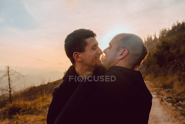 Feliz casal homossexual abraçando no caminho na floresta em dia ensolarado — Fotografia de Stock