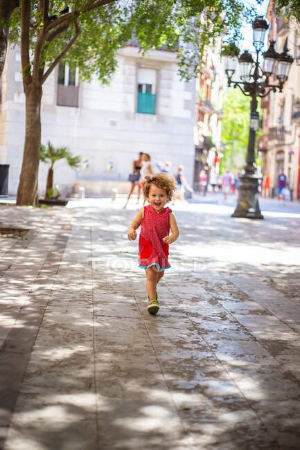 Feliz chica divertida corriendo en la calle de asfalto entre los edificios en verano - foto de stock