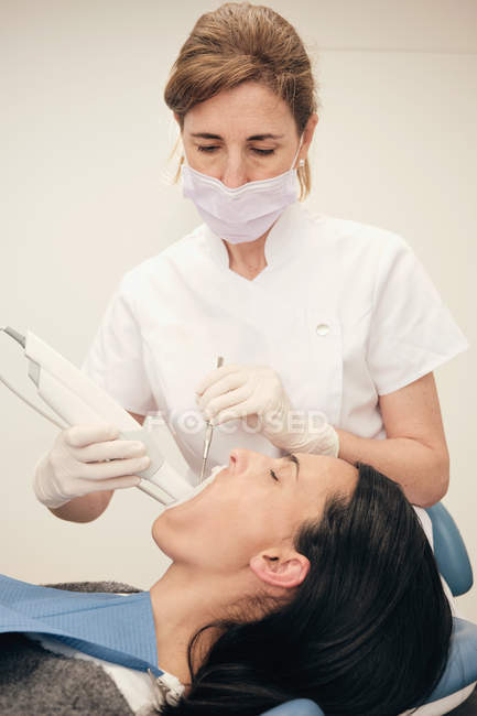 Frau in Handschuhen und Maske mit modernen Geräten zur Untersuchung der Zähne einer Patientin in der Zahnarztpraxis — Stockfoto