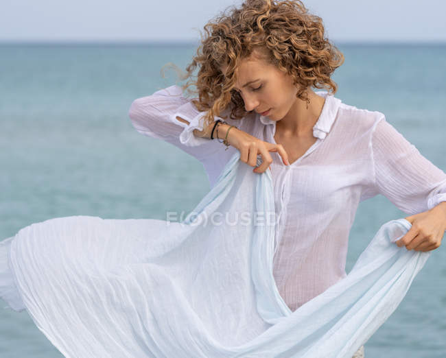 Giovane donna pensierosa guardando giù e tenendo sciarpa vicino alla superficie dell'acqua di mare — Foto stock