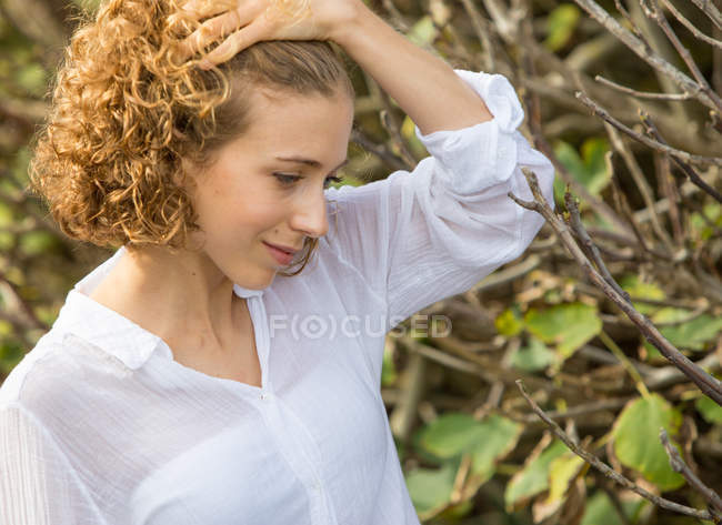 Jovem mulher sonhadora de pé perto de ramos secos de arbusto no fundo borrado — Fotografia de Stock