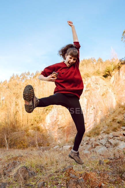 Молодая хипстерша с поднятой рукой слушает музыку по мобильному телефону и танцует на природе — стоковое фото