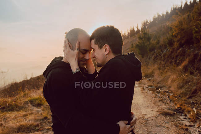 Vista lateral de la pareja homosexual abrazándose en el camino en el bosque en un día soleado - foto de stock