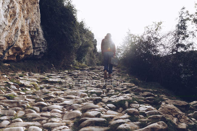 Vue arrière de femme occasionnelle cas de transport et de marcher sur des rochers de ruisseau clair de l'eau dans la nature — Photo de stock