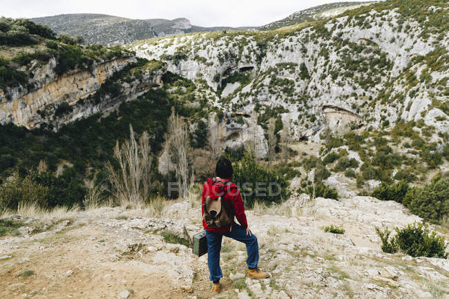 Back view of traveling woman with backpack sitting on high rocky cliff observing beautiful valley — Stock Photo