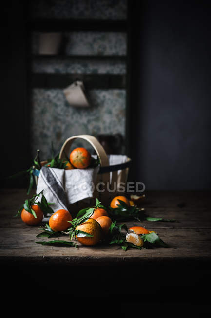 Ripe mandarins with leaves and basket on rough wooden table — Stock Photo
