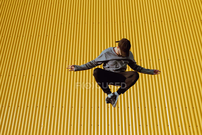 Bonito barbudo cara na roupa da moda pulando contra a parede amarela do edifício moderno — Fotografia de Stock