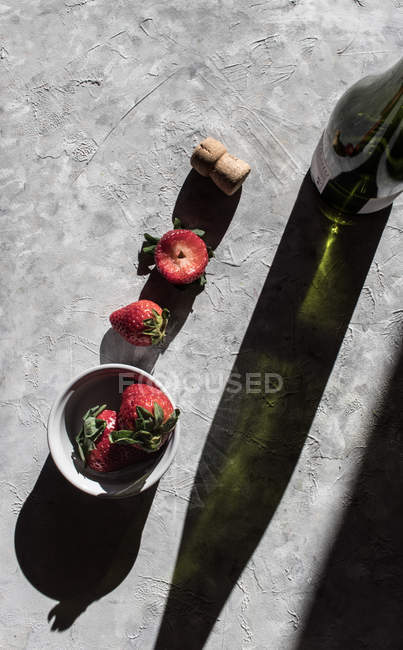 Fresh strawberries in bowl and on grey surface with bottle of wine — Stock Photo