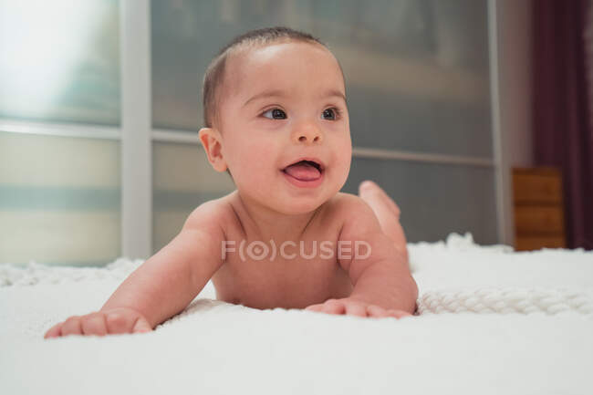 Funny little naked newborn looking away and lying on bed in room — Stock Photo